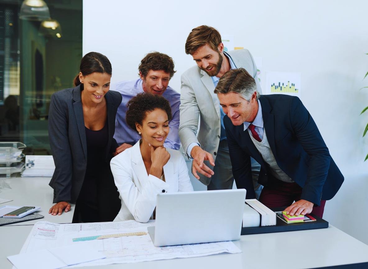 Equipe de profissionais reunida em torno de um laptop discutindo mensagens de voz transcritas no PABX em nuvem